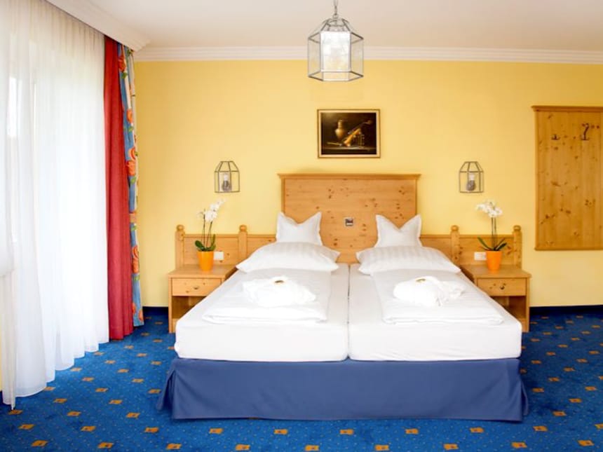 Gemütliches Hotelzimmer mit Doppelbett, gelb gestrichenen Wänden und blauen Teppichboden.