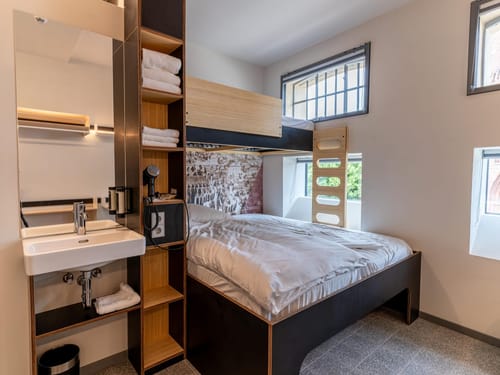 Hotelzimmer in einem ehemaligen Gefängnisgebäude mit einem Etagenbett aus dunklem Holz, weißer B