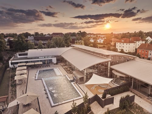 Der Wellnessbad-Komplex aus der Vogelperspektive – der Außenbereich mit Pool und Liegedeck erstrahlt im warmen Licht des Sonnenuntergangs.