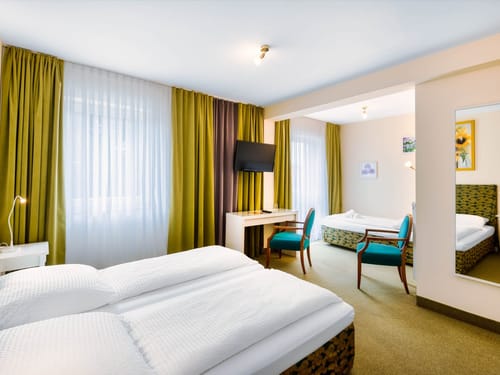 Helles und geräumiges Hotelzimmer mit Doppelbett, Einzelbett, Schreibtisch und stilvoller Dekoration in Grün- und Türkistönen