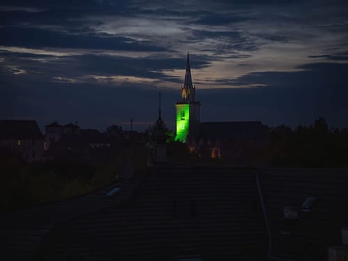 Grün beleuchteter Kirchturm in der Abenddämmerung