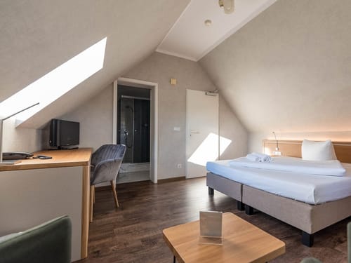 kleines Doppelzimmer unter dem Dach mit Doppelbett, Schreibtisch, Stuhl und TV