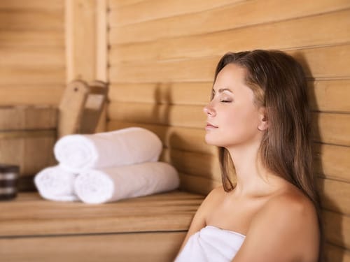 Frau entspannt in einer Sauna mit Handtüchern im Hintergrund.