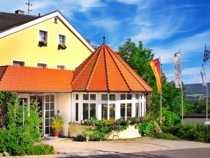 Traditionelles bayerisches Gasthaus mit rotem Dach und Landesfahnen