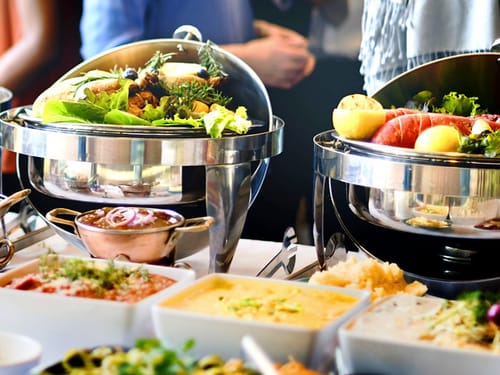 Elegantes Buffet mit abwechslungsreichen Speisen und Salaten in glänzenden Warmhaltebehältern.