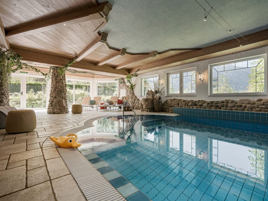 Luxus-Innenpool mit Panoramafenstern und gemütlichen Liegen in natürlichem Ambiente.