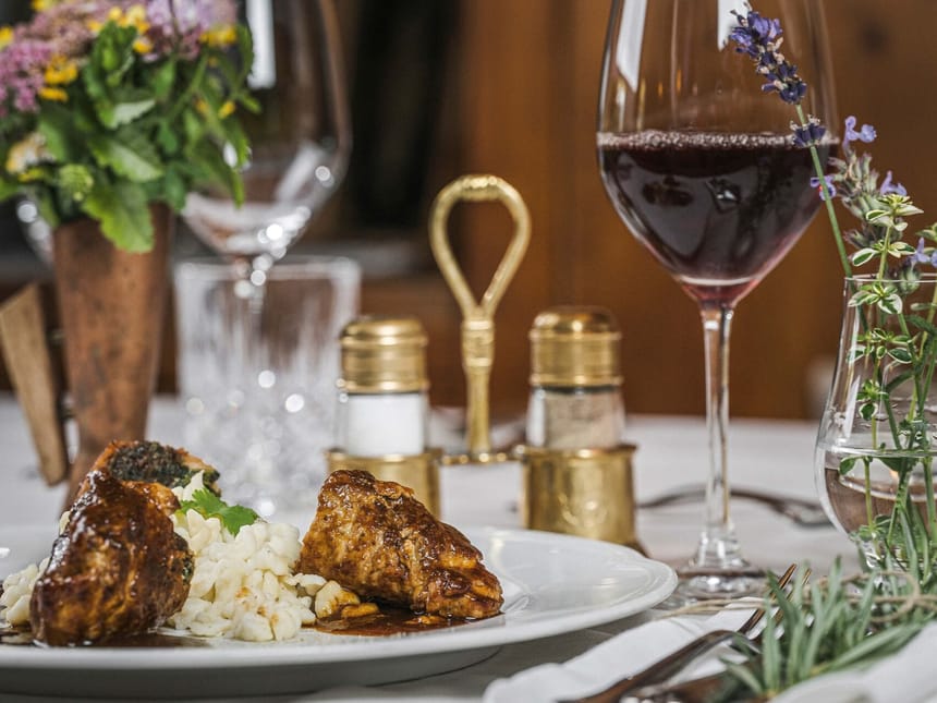 Leckeres Gericht mit Fleisch und Spätzle, serviert mit einem Glas Rotwein auf einem elegant gedeckten Tisch.