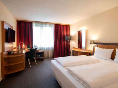 Modernes Hotelzimmer mit Doppelbett, Schreibtisch und rotem Vorhang