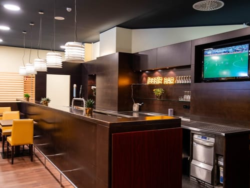 Moderne Innenansicht einer stilvollen Bar mit Holzdekor und Sportübertragung auf einem Bildschirm.