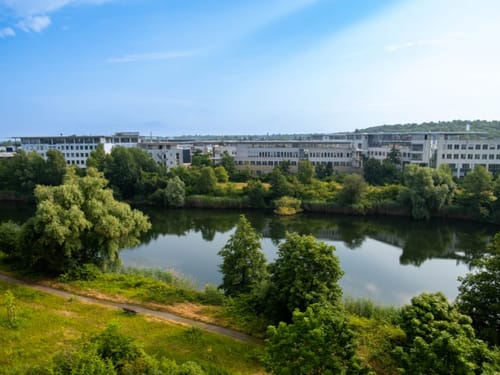Moderne Bürogebäude an einem Flussufer mit grüner Landschaft.