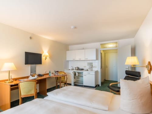 Gemütliches Hotelzimmer mit Doppelbett, Schreibtisch und kleiner Küchenzeile.