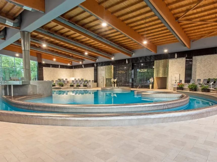 Luxuriöser Innenpoolbereich in einem modernen Hotel mit Holzdecken und Liegestühlen.