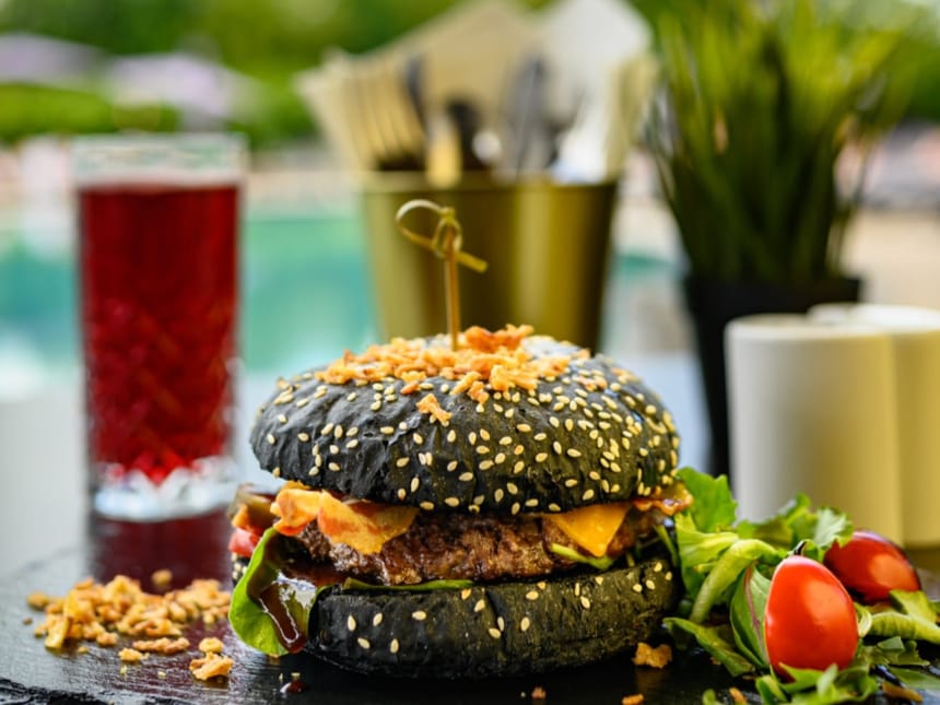 Gourmet-Burger mit schwarzem Sesambrötchen und Beilagensalat neben einem Glas Getränk