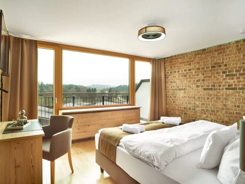 Modernes Hotelzimmer mit Backsteinwand und großen Fenstern mit Ausblick auf die Natur.