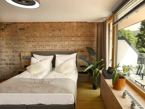 Modernes Hotelzimmer mit Backsteinwand, gemütlichem Doppelbett und großen Fenstern mit Naturblick