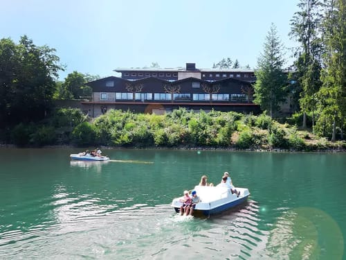 Familie genießt Tretbootfahrt auf einem idyllischen See vor einem Hotel.
