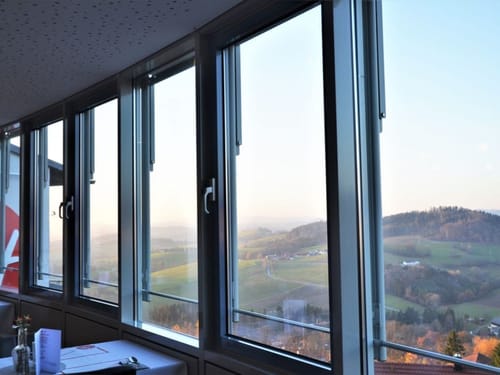 Blick aus einem großen Fenster auf eine hügelige Landschaft bei Sonnenuntergang.