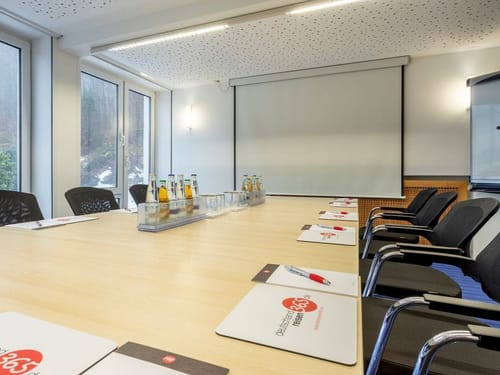 Moderner Konferenzraum mit großem Holztisch und Stühlen vorbereitet für ein Meeting, mit Notizblöcken und Wasserflaschen.