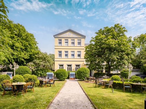 Historisches Haus mit gepflegtem Garten und Gartenmöbeln an einem sonnigen Tag.