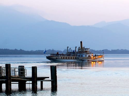Dampfschiff auf einem See vor Bergkulisse im Sonnenuntergang