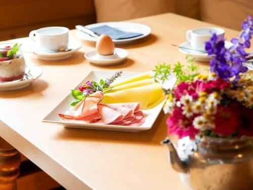 Frühstückstisch mit Aufschnitt, Käse, gekochtem Ei und Blumenarrangement.