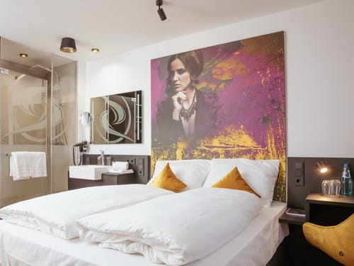 Entdecken Sie unser modernes Hotelzimmer, das mit einem einzigartigen Kunstwerk und einem komfortablen Doppelbett ausgestattet ist. Perfekt für einen erholsamen Aufenthalt.
