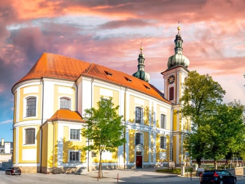 Barockkirche bei Sonnenuntergang mit zwei Türmen und dramatischem Himmel.