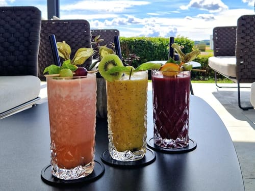 Drei verschiedene Fruchtcocktails mit frischem Obst auf einem Tisch im Freien.