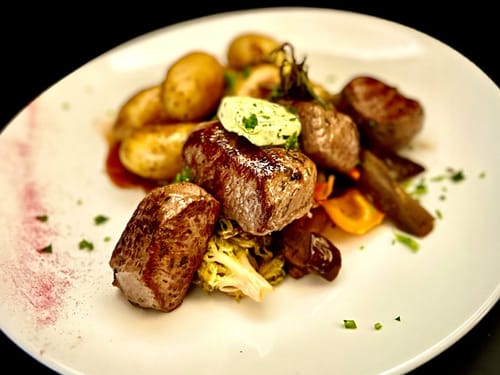 Köstliches Rinderfilet mit frischem Gemüse und Kartoffeln auf weißem Teller.