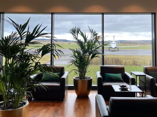 Elegante Flughafenlounge mit Ledersesseln und Blick auf ein geparktes Privatflugzeug.