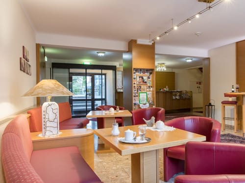 Gemütlicher Sitzbereich in einem Hotel mit roten Sesseln und Holztischen.