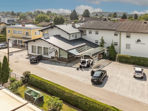 Luftaufnahme eines Gebäudes mit Parkplatz und umliegender Landschaft.
