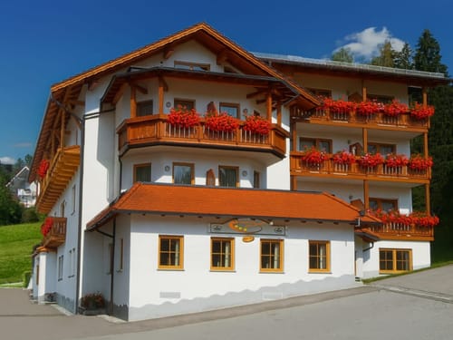 Entdecken Sie dieses idyllische Alpenhotel mit seinen traditionellen Holz-Balkonen und leuchtend roten Geranien. Perfekt für einen erholsamen Urlaub in den Bergen.