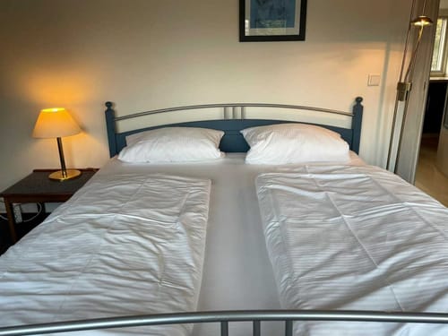 Gemütliches Doppelbett mit weißer Bettwäsche und Nachttischlampe in einem Schlafzimmer.