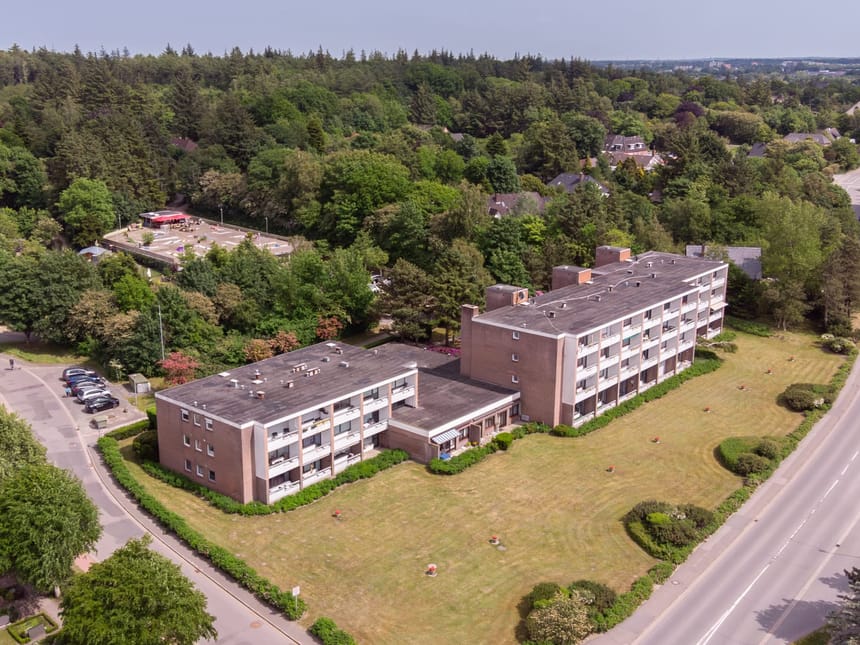 Luftaufnahme eines Wohngebäudes im Grünen, umgeben von Bäumen und einer Straße.