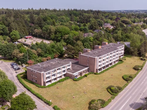 Luftaufnahme eines Wohngebäudes im Grünen, umgeben von Bäumen und einer Straße.