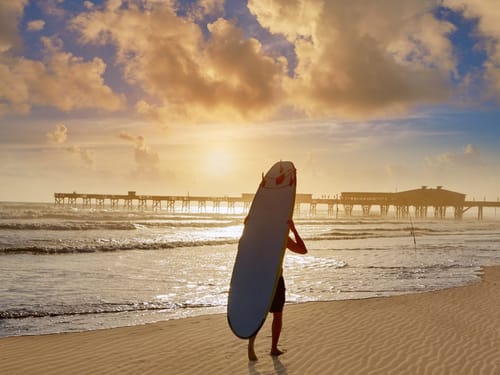 Surfer bei Sonnenuntergang am Strand mit Blick auf den Pier