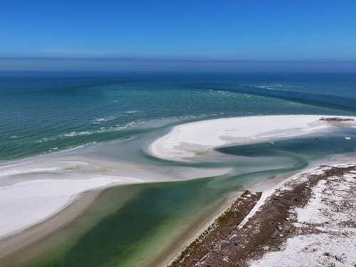 Luftaufnahme eines weißen Sandstrandes und einer türkisblauen Lagune am Meer.