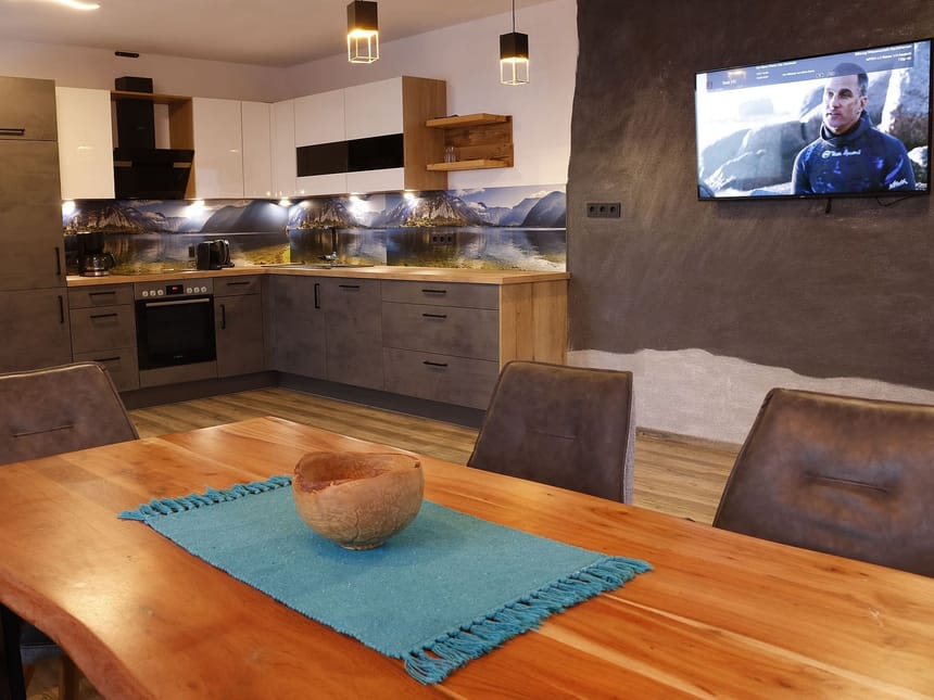 Moderne Küche mit Eckspüle, grauen Schränken, großem Holztisch und TV.