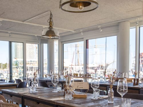 Stilvoll gedeckter Tisch in einem Restaurant mit Blick auf einen Yachthafen.