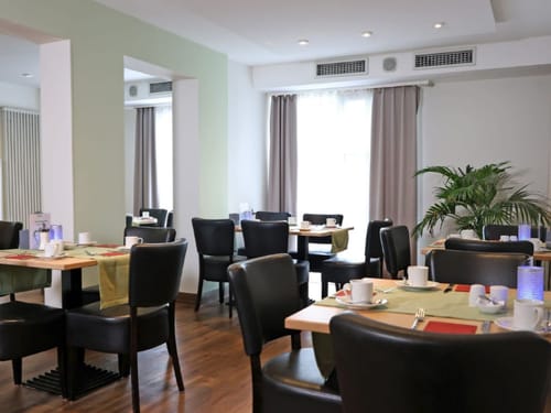 Gemütliches Frühstücksrestaurant mit gedeckten Tischen und Pflanzen im Hintergrund.