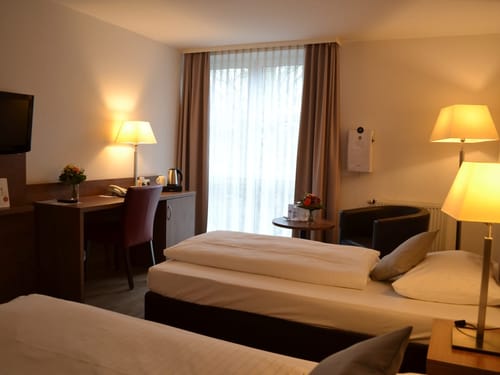 Gemütliches Hotelzimmer mit zwei Einzelbetten, Schreibtisch und Sessel.