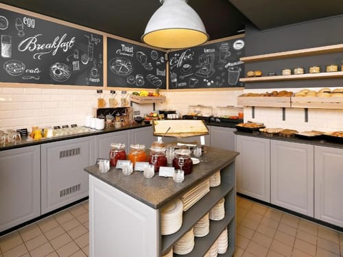 Kontinentales Frühstücksbuffet mit Brot, Gebäck, Marmeladen und Müsli in modernem Café.