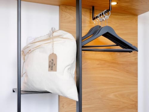 Offener Kleiderschrank mit schwarzen Kleiderbügeln und einer Tasche mit der Aufschrift "Frische zum Kuscheln".