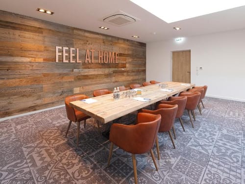 Moderner Konferenzraum mit rustikalem Holztisch und Ledersesseln, dekoriert mit der Aufschrift "Feel at Home" an der Wand.