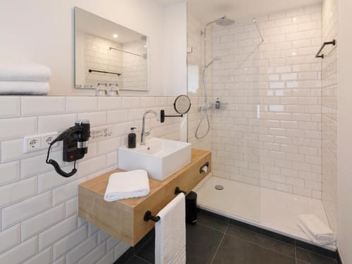 Entdecken Sie ein elegantes Badezimmerdesign mit einer begehbaren Dusche, weißen Kacheln und einem eleganten Waschbecken mit Holzunterschrank. Perfekt für moderne Wohnungen und Häuser, die Stil und Funktionalität kombinieren.