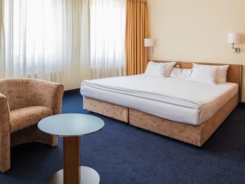 Helles und gemütliches Hotelzimmer mit Doppelbett, Sessel und kleinem Tisch