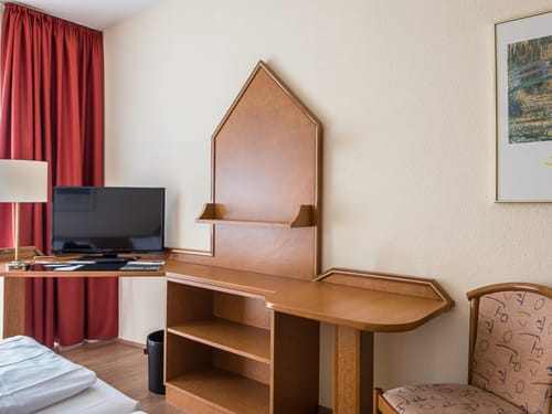 Hotelzimmerbereich mit Schreibtisch, Fernseher und rotem Vorhang.