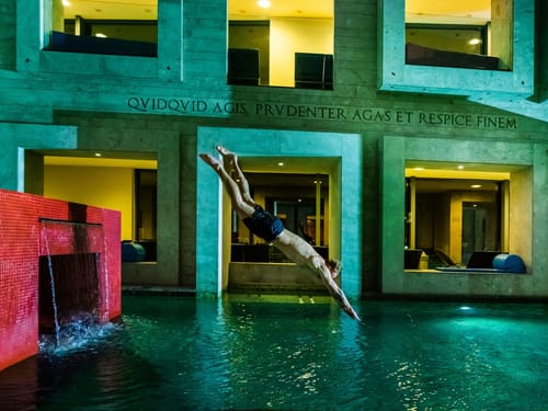 Person im Flug beim Kopfsprung in einen beleuchteten Pool bei Nacht.