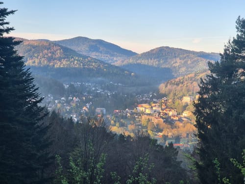 Blick auf einen malerischen Ort umgeben von bewaldeten Hügeln im Sonnenlicht.